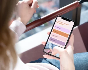 Kupla Socialin nettisivujen etusivun palvelulistaus mobiililaitteella. Nuori nainen katselee puhelinta, jonka ruudulla Kupla Socialin palvelut ovat.